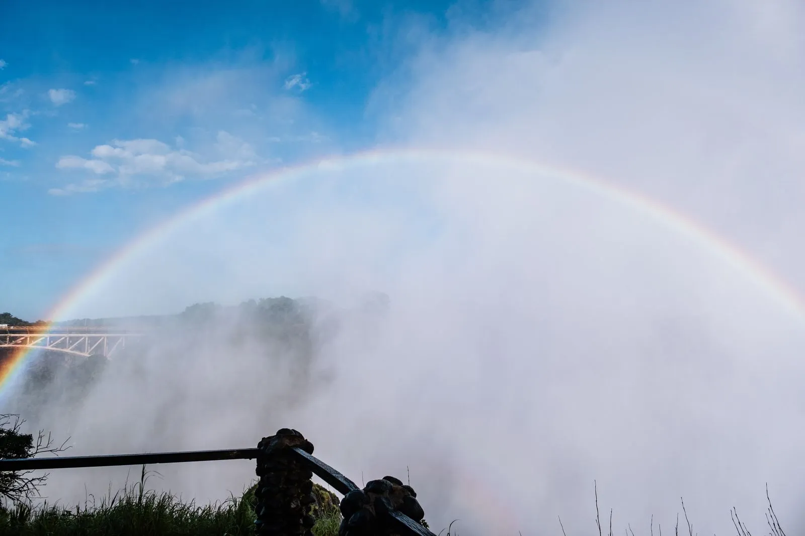 Rainbow arching through the spray, Victoria Falls Bridge at the left edge