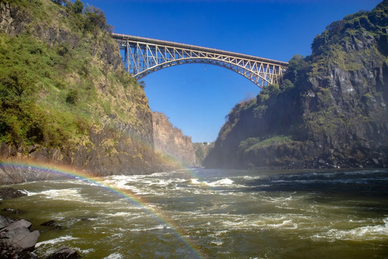 Victoria Falls Bridge over the gorge, seen from the river with a rainbow