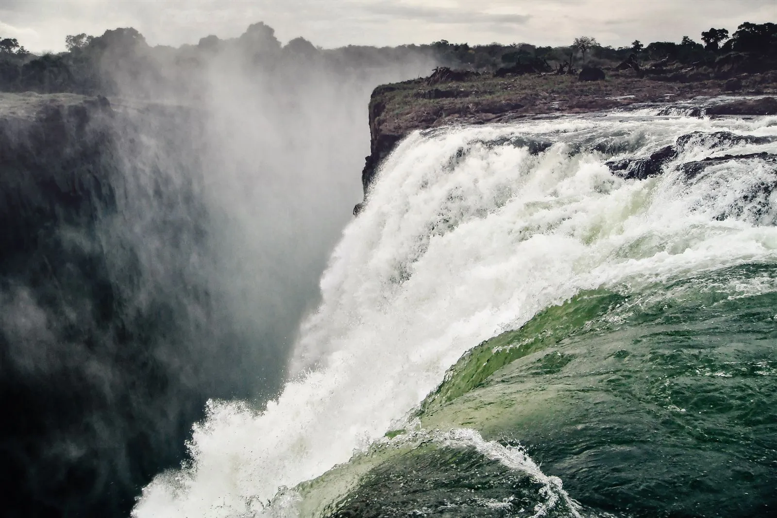 Green water curling over the lip of the falls into rising spray