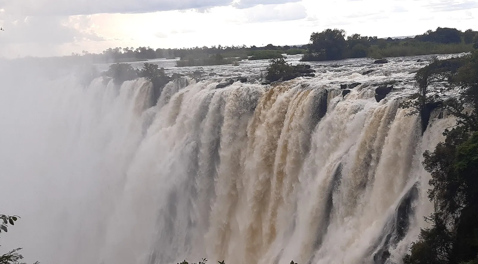Brown floodwater pouring over the falls in April, islands upstream