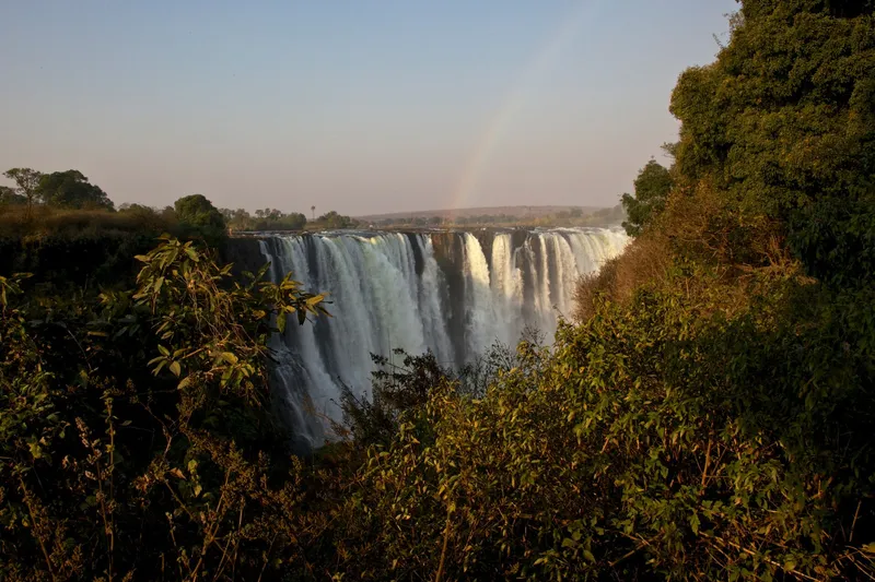 The falls seen through dry-season bush, a faint rainbow in the spray