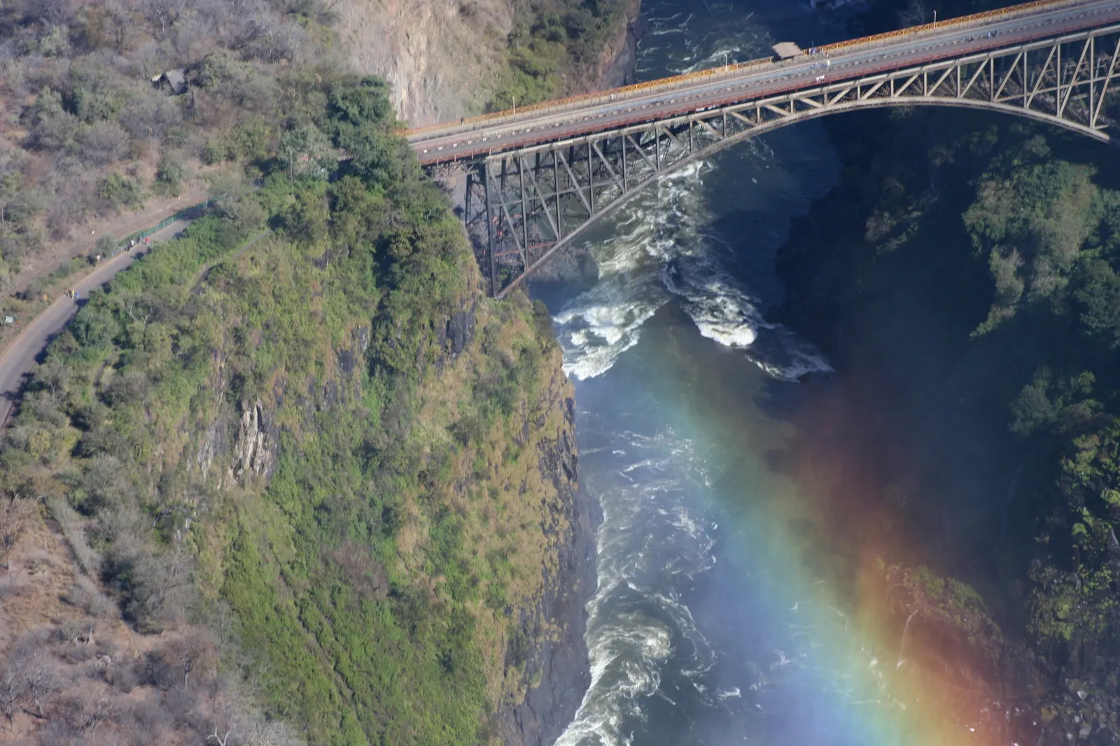 Victoria Falls Bridge from the air, rapids below and a rainbow in the spray