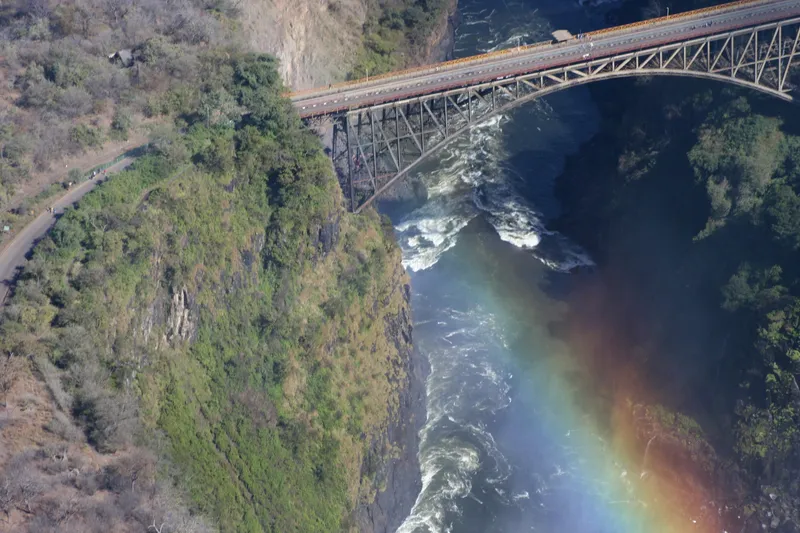 Victoria Falls Bridge from the air, rapids below and a rainbow in the spray