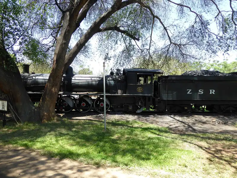 Old ZSR steam locomotive no. 156 and its coal tender under a tree in Livingstone