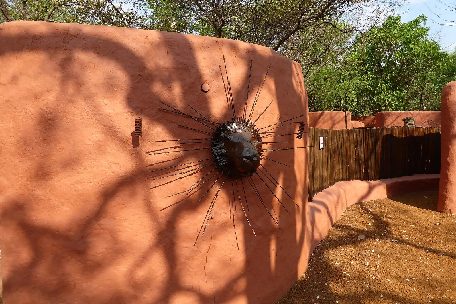 Lion-head sculpture with wire rays on a red clay wall in Livingstone