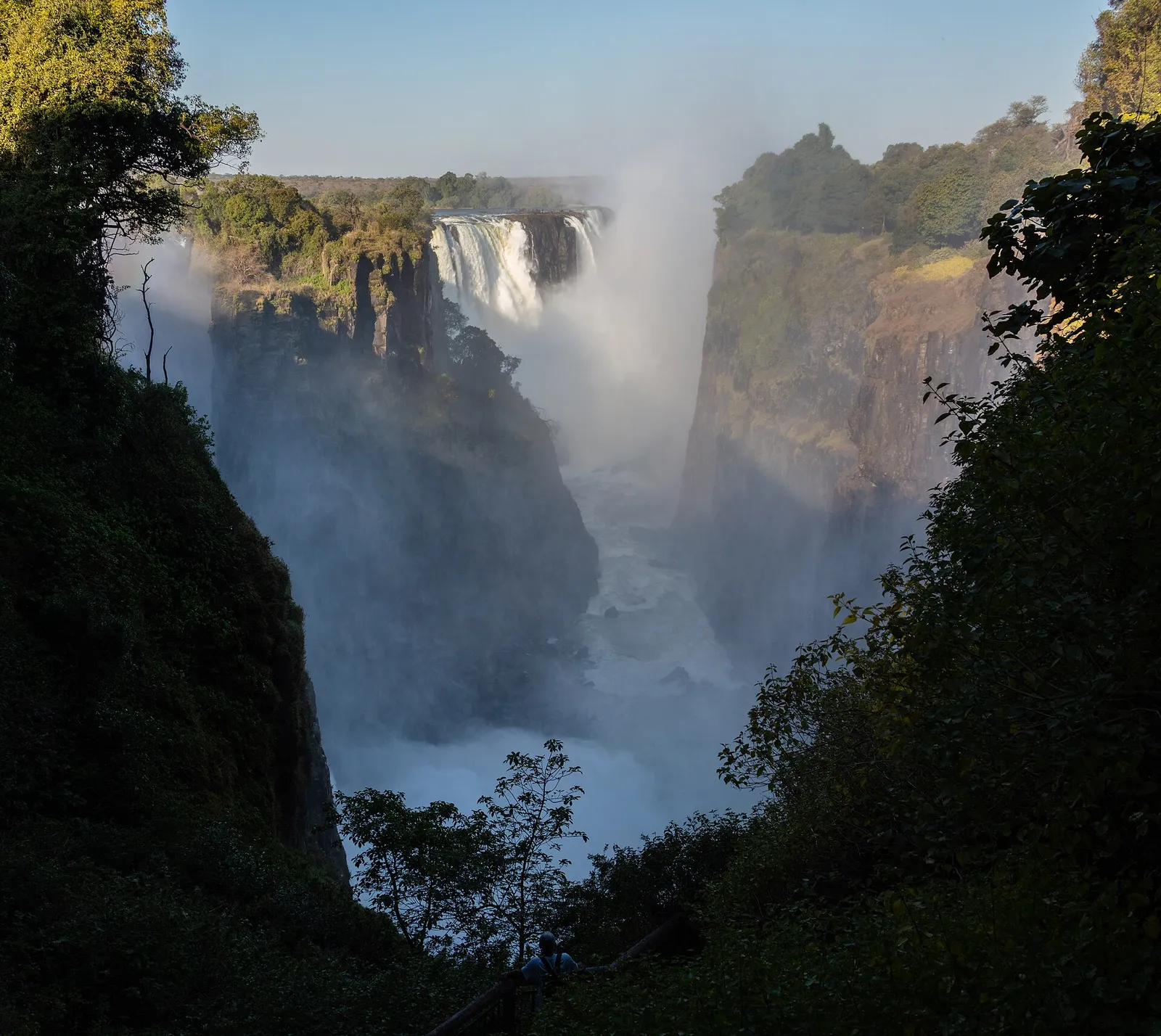 Spray rising from the falls at the end of a deep, tree-lined gorge