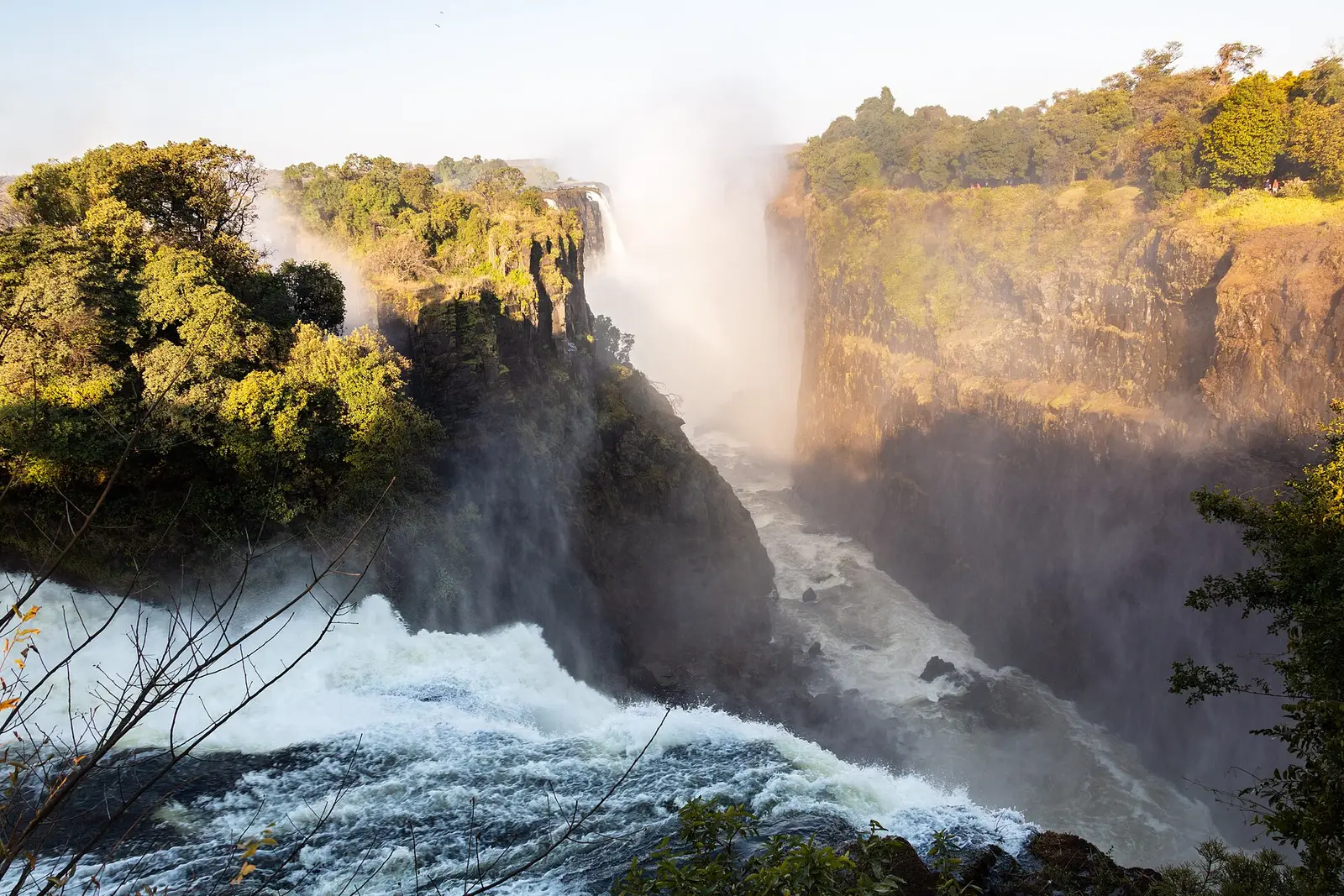 Water racing into the gorge below the falls, cliffs lit by low sun